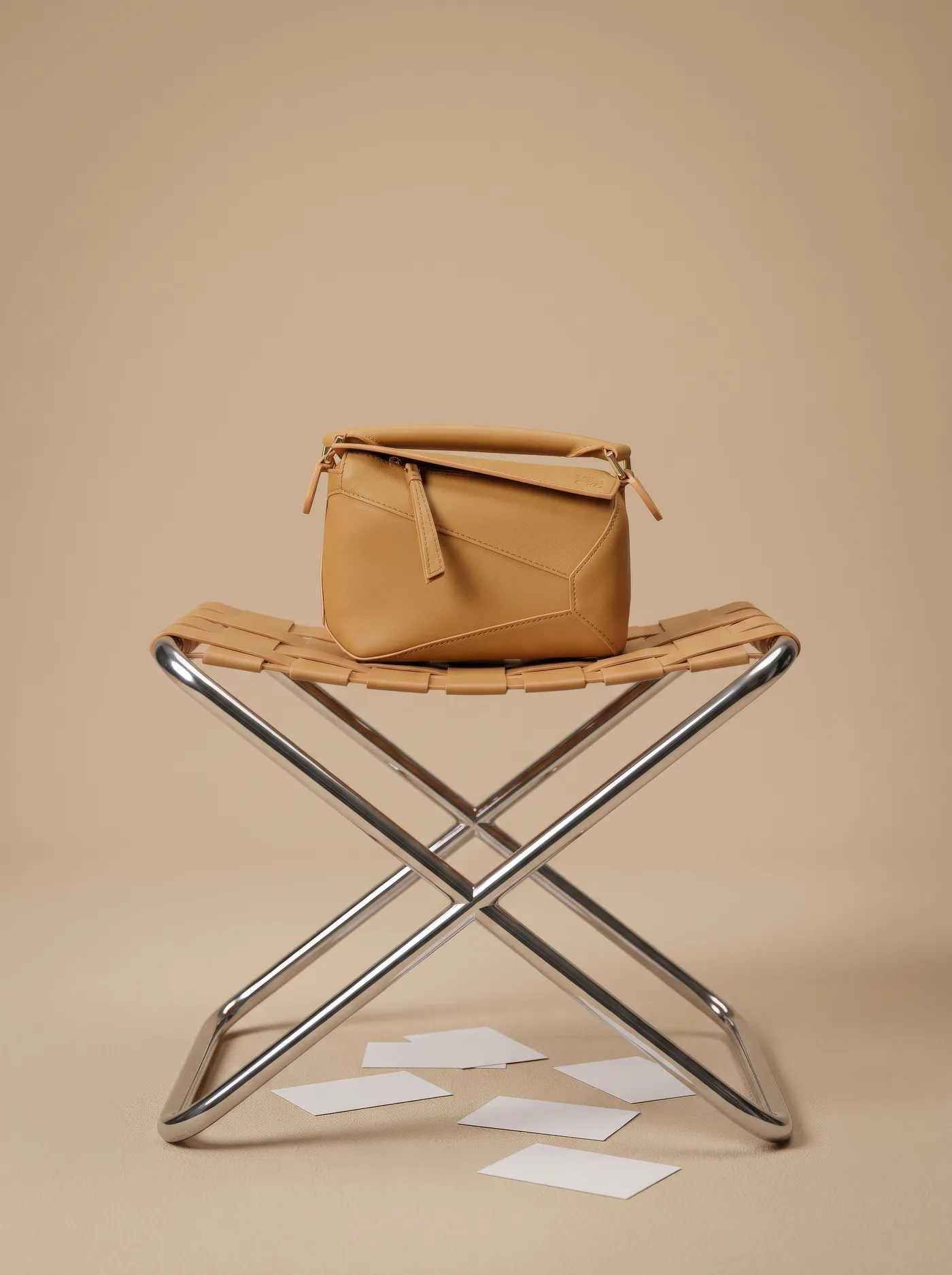 Folded leather bag with a curved handle on a chrome and woven-leather stool